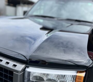 ヘッドライトやフロントグリルが映る、カーコーティング後の黒い車のボンネット部分の光沢感