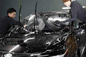 黒い車のフロント部分を2人のスタッフがスポンジで丁寧に手洗いしている様子