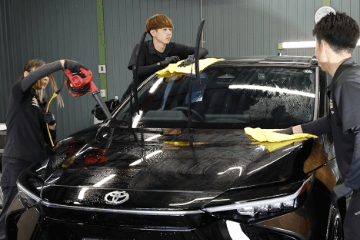 黒い車のボンネットとフロントガラスを3人のスタッフが拭き上げとブロワーで仕上げている様子