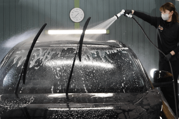 泡立った黒い車のフロントガラスにスケール除去剤をリンスで洗い流している様子