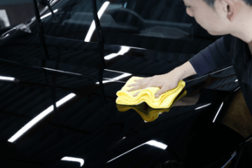 黒い車のボンネットを黄色いクロスで丁寧に拭き上げる男性スタッフの様子