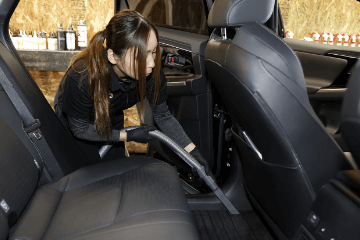 車の後部座席で掃除機を使い、フロアを丁寧に清掃している女性スタッフの様子